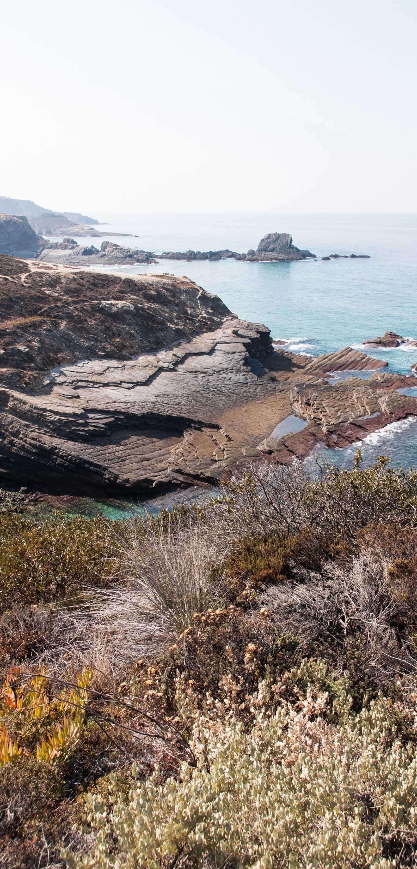 Há um homem em pé em uma colina com vista para o oceano (costa, penhasco, mar, oceano, praia)