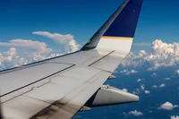 Vista de uma asa de avião contra um céu azul vibrante com nuvens