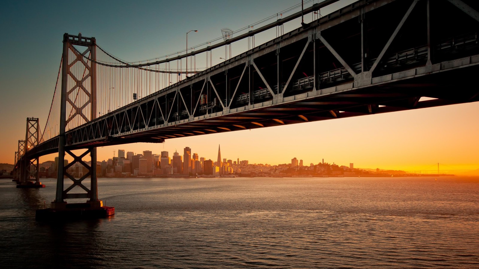 Арочный вид на мост над водоемом с городом на фоне (мост окленд бэй, oakland bay bridge, мост золотые ворота, golden gate bridge, подвесной мост)