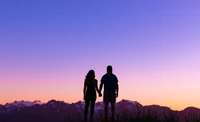 Silhouette romantique de amoureux se tenant par la main contre un lever de soleil sur des montagnes glaciaires