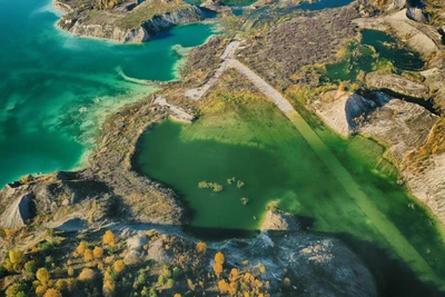 Аэроснимок яркого водотока, извивающегося через пересеченный ландшафт, окруженный разнообразным рельефом и яркой листвой.