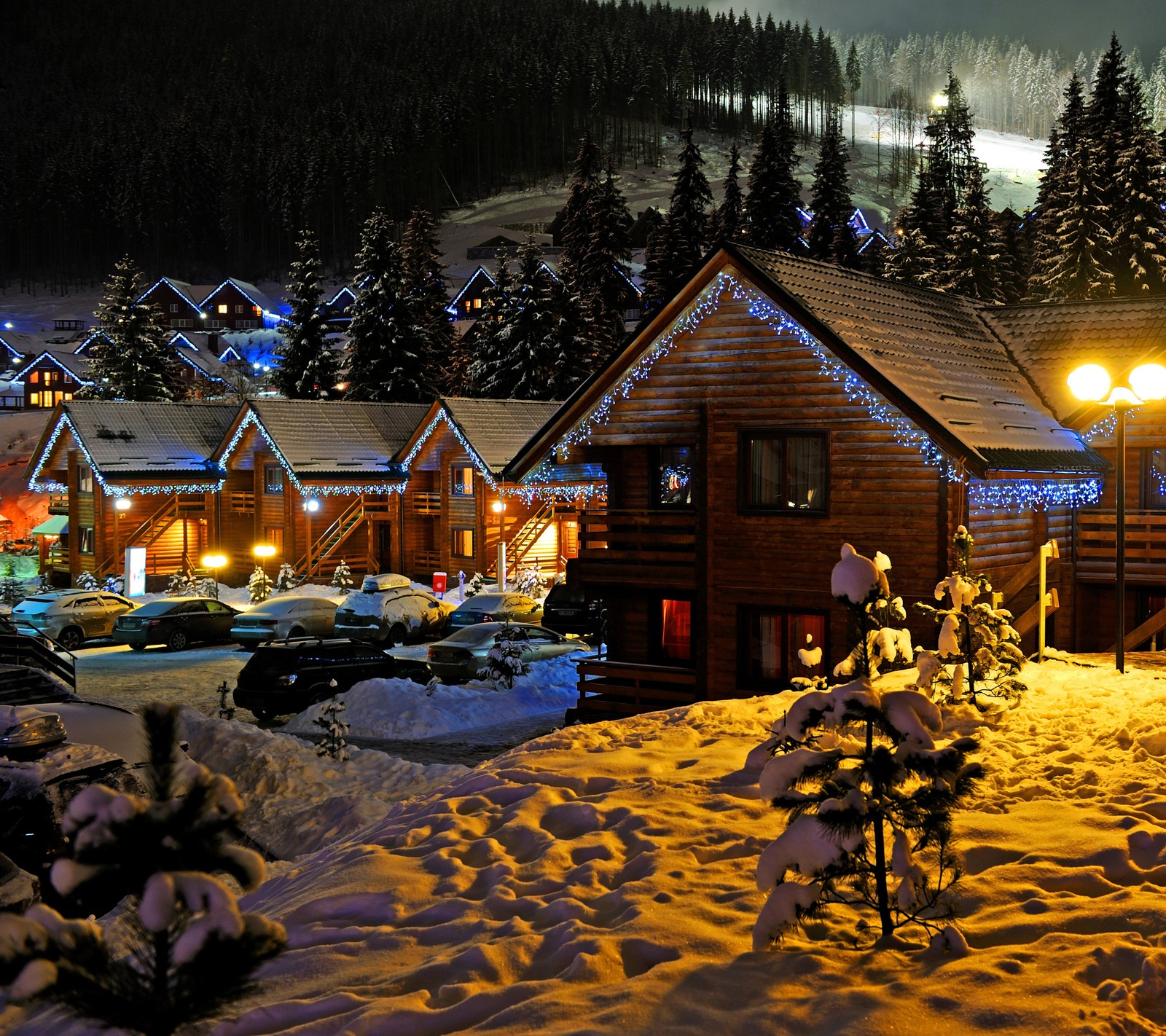 Schneebedeckte nachtszene mit einer hütte, weihnachtslichtern und bäumen (festlich, feiertag, lichter, winter)