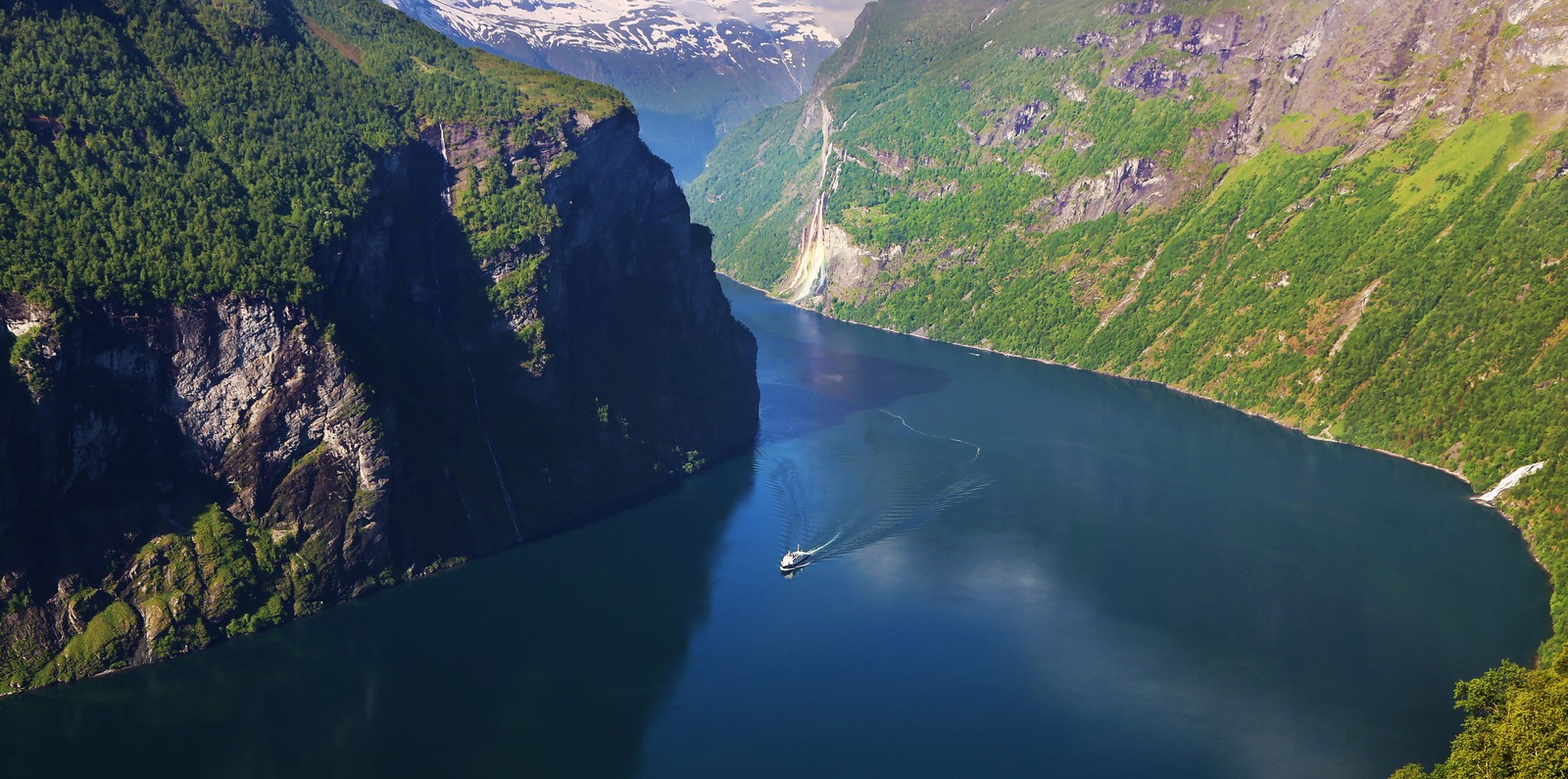 Un bateau arabe dans un grand plan d'eau entouré de montagnes (fjord, stockholm, geiranger, voyage, hauts plateaux)