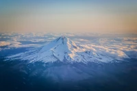 Majestosa Montanha Hood se erguendo acima de um mar de nuvens ao pôr do sol, exibindo seu pico coberto de neve e terreno acidentado.