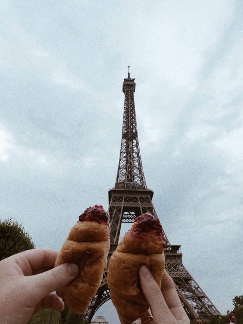 Кто-то держит две выпечки перед эйфелевой башней (париж, paris, эйфелева башня, круассан, шамп де марс)