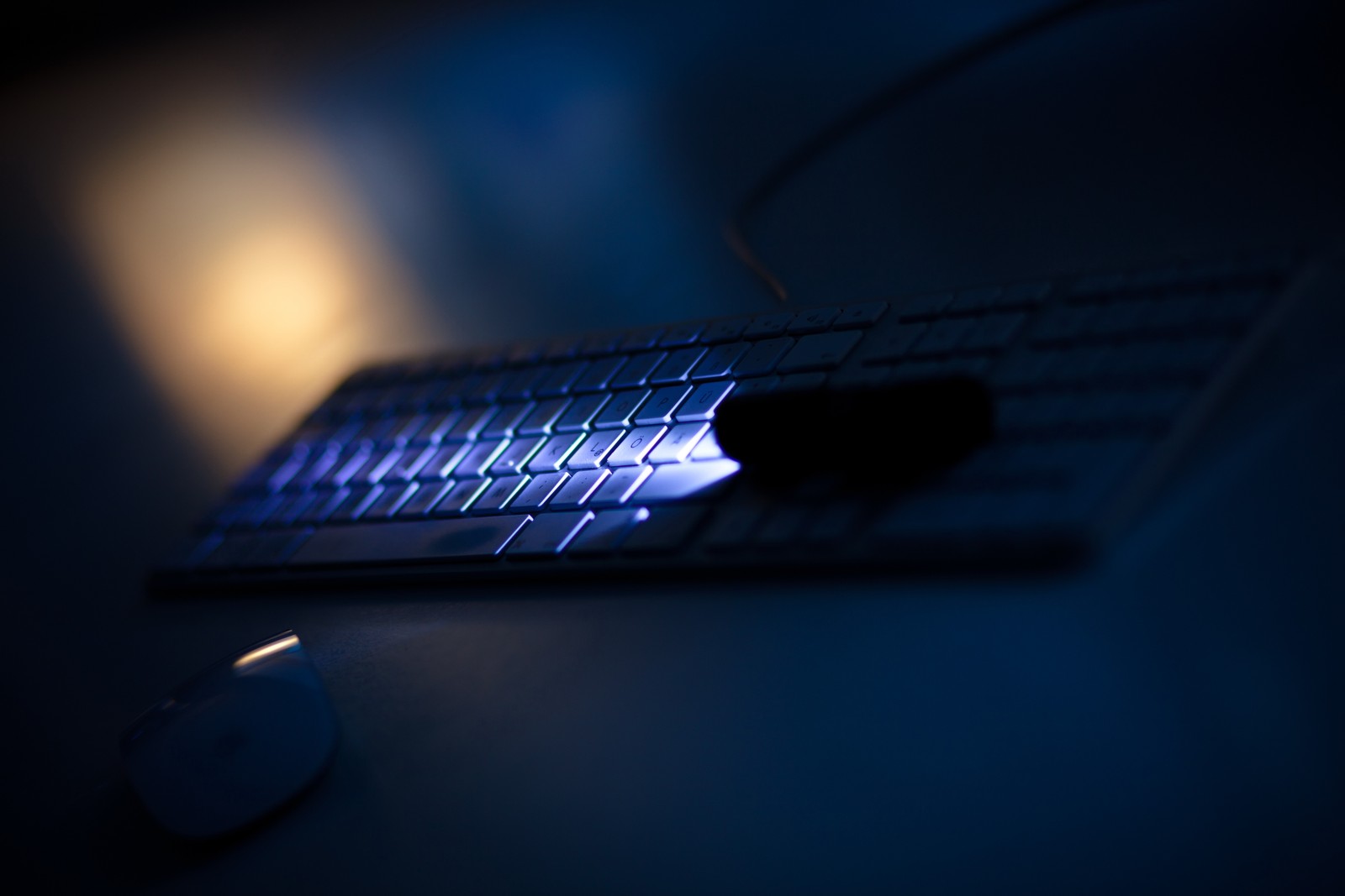 Hay un teclado y un ratón en una mesa con una luz encendida (ligero, noche, iluminación, tecnología, oscuridad)