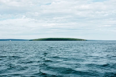 Calm waters reflecting a serene sky, with a lush green islet on the horizon.