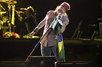 Axl Rose leidenschaftlich auf der Bühne, in eine brasilianische Flagge gehüllt, während eines lebhaften Konzerts.