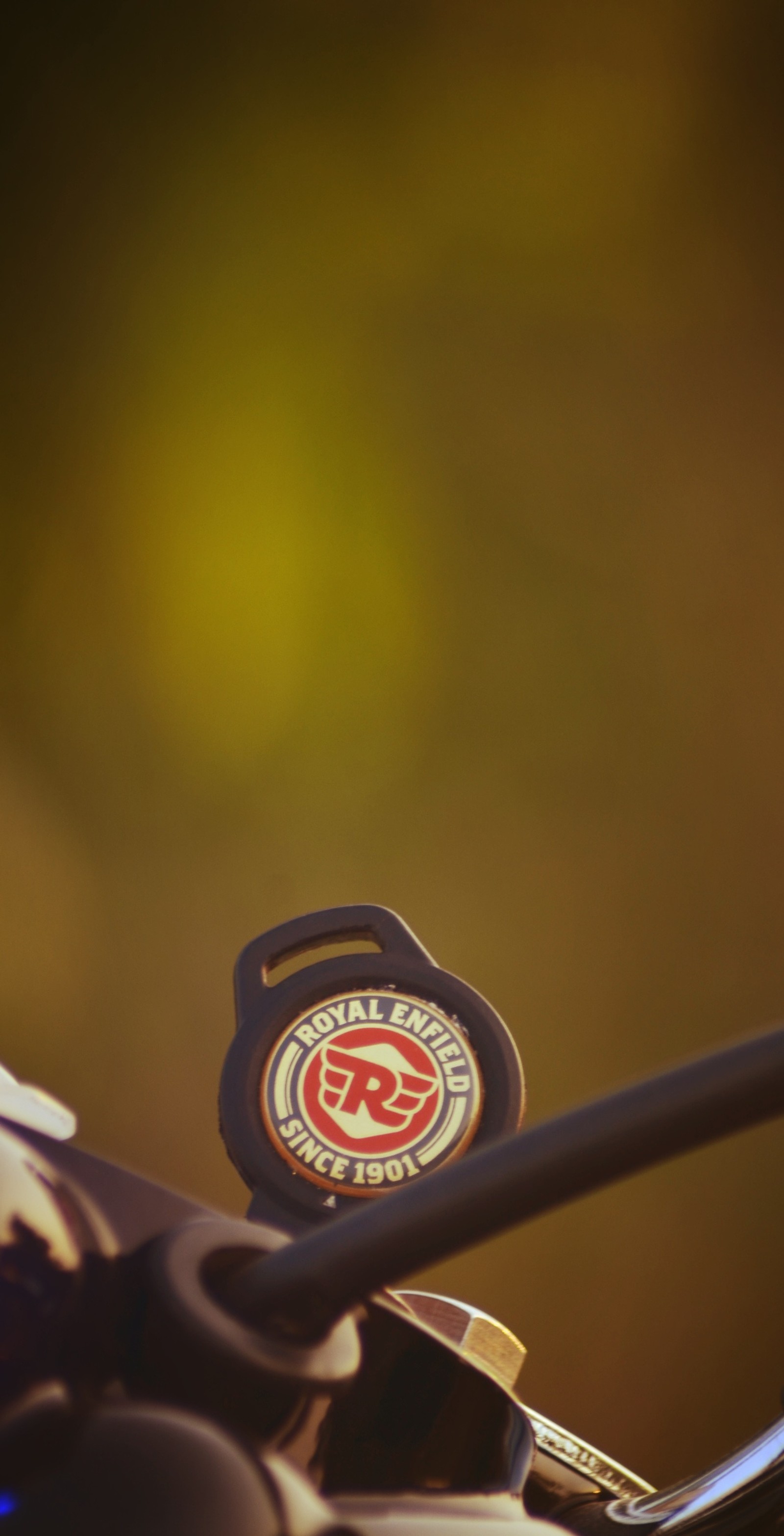 There is a close up of a motorcycle handlebar with a badge on it (enfield, keys, royal, royal enfield, royal enfield keys)