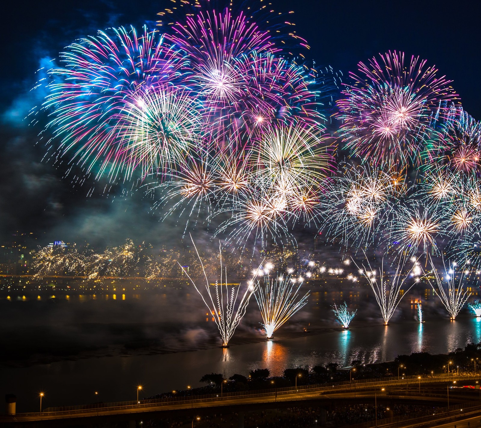 Fireworks are lit up over a city and a river (blue, fireworks, happy, new year, pink)