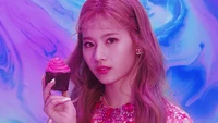 Minatozaki Sana sosteniendo un cupcake contra un fondo vibrante