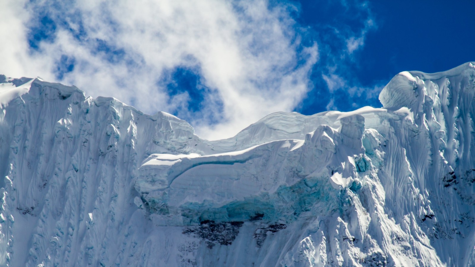 Una montaña cubierta de nieve con algunas nubes en el cielo (casquete polar, formas montañosas, forma glaciar, hielo, montaña)