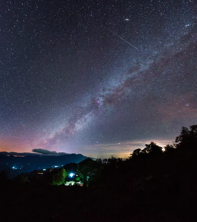 Ein atemberaubender Blick auf die Milchstraße, die in einem sternenfüllten Nachthimmel schimmert, umgeben von fernen Bergen und einem Hauch von atmosphärischem Glühen.