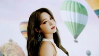 Jisun de fromis_9 pose élégamment devant un arrière-plan de ballons à air chaud colorés, dégageant une aura charmante et vibrante.