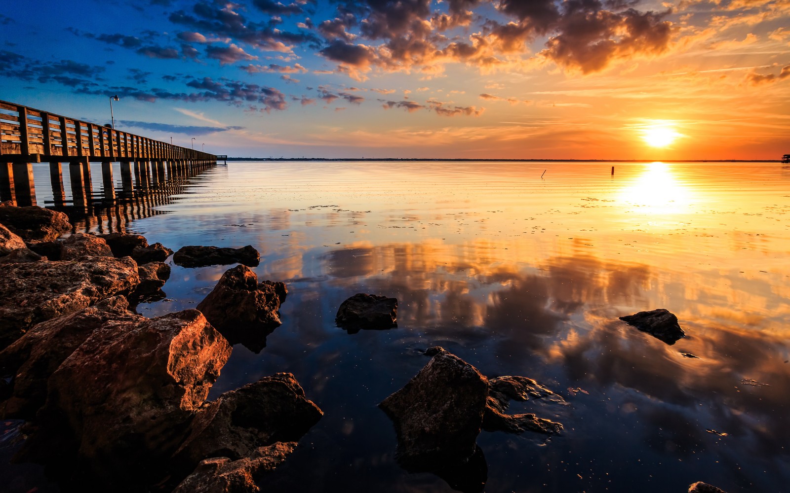 A view of a pier with rocks and water at sunset (reflection, water, horizon, sea, shore)