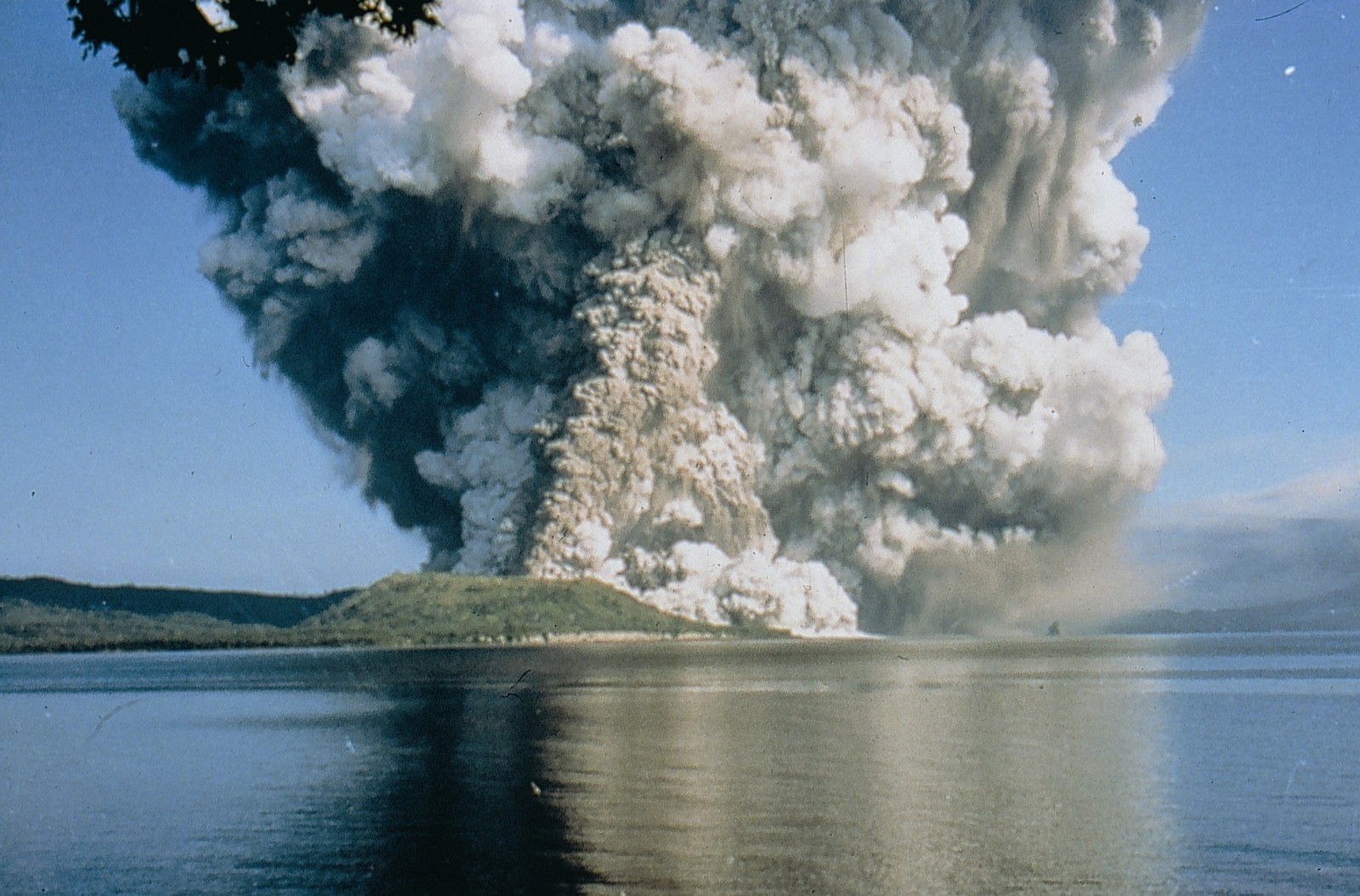 Un panache de fumée s'élevant d'un lac avec un bateau dans l'eau (volcan, nuage, fumée, forme volcanique, types déruptions volcaniques)