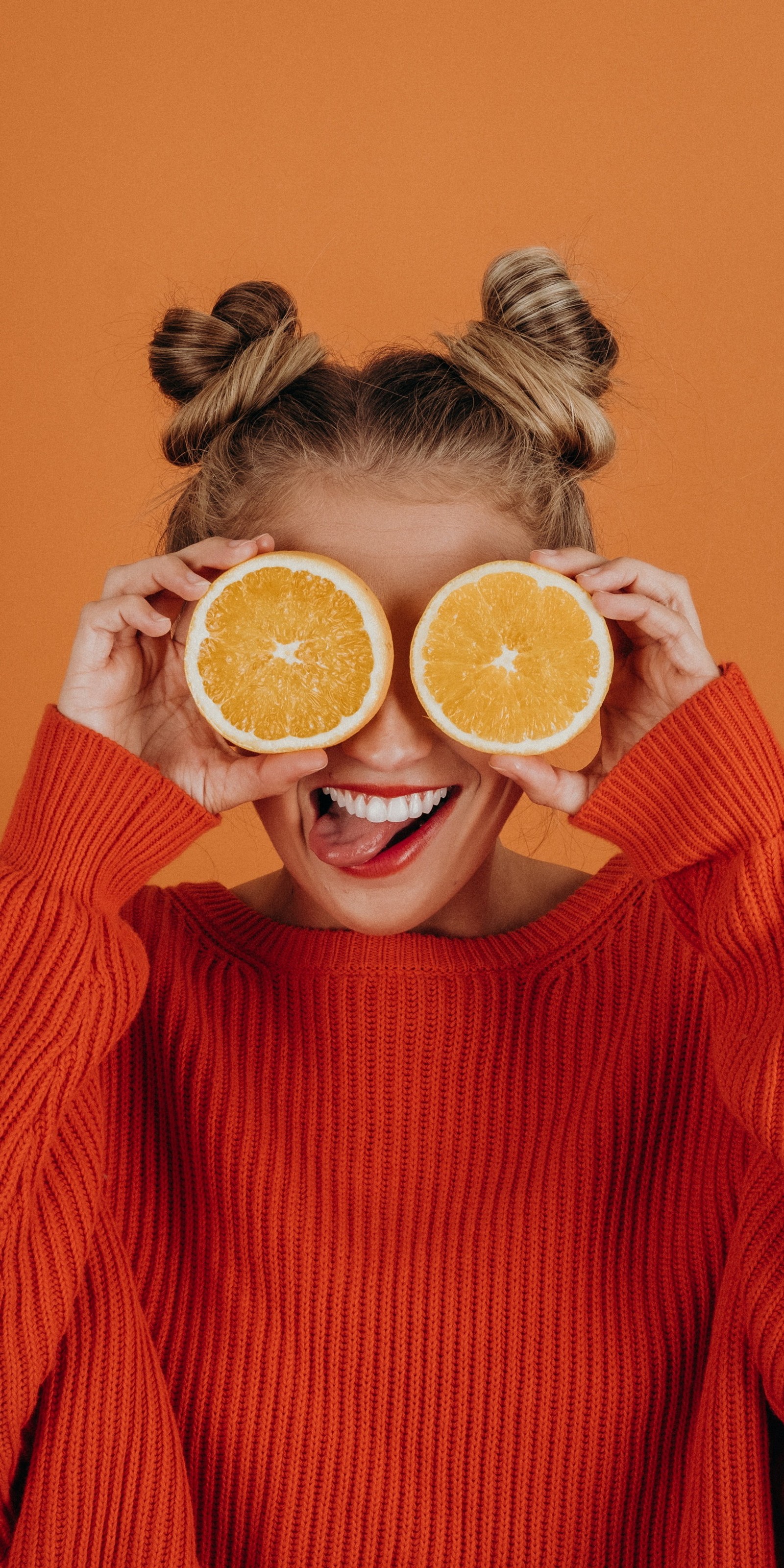 Frau, die zwei orangenscheiben vor den augen hält (porträt, orangensaft, saft, orange, essen)