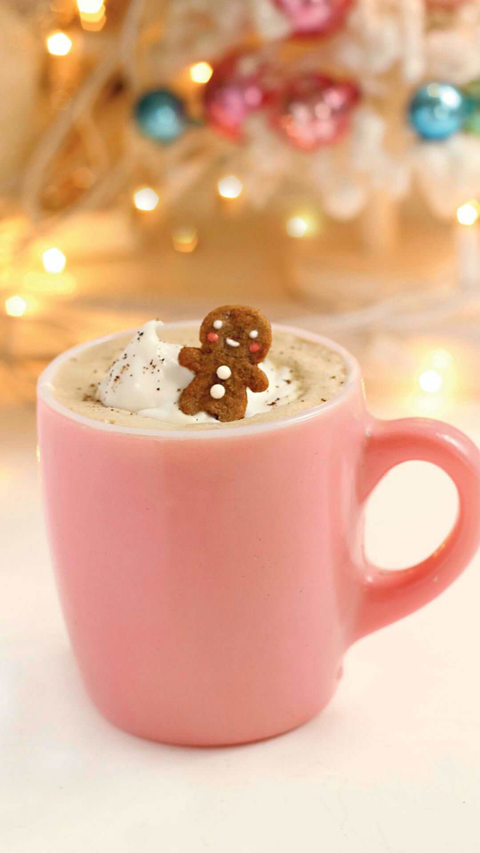 Il y a une tasse rose avec une boisson et une décoration en pain d'épice. (noël, coco, décorations, pain dépice)