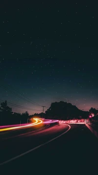 Estrada noturna com luzes automotivas contra um céu estrelado