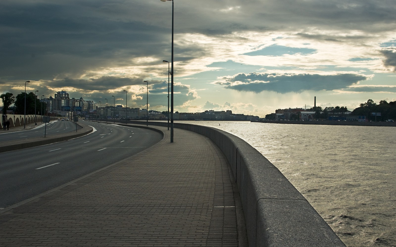 There is a street sign on the side of a road near the water (neva river, cloud, water, horizon, road)