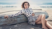 Emilia Clarke in einer stilvollen Strandumgebung, mit einem schicken Outfit vor einer malerischen Ozeankulisse.