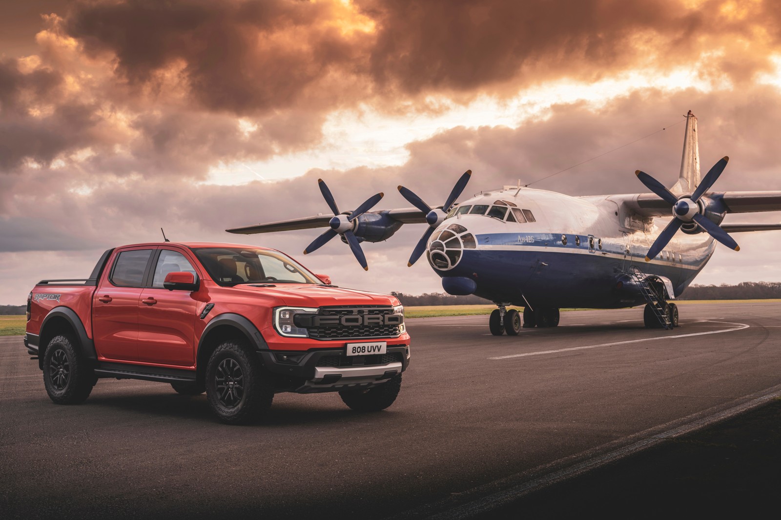 Un camión rojo árabe estacionado junto a un avión en una pista de aterrizaje (ford ranger raptor, 2023, 5k, coches, fondo de pantalla 4k)