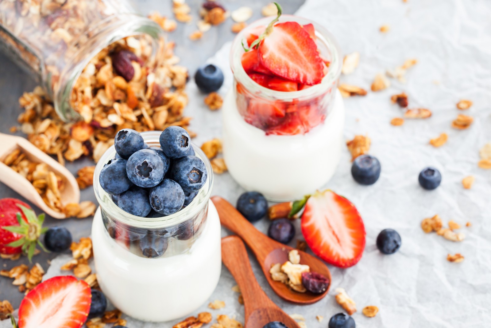 Il y a deux pots de yaourt avec des fraises et des myrtilles (petit déjeuner, muesli, myrtille, baie, dessert)