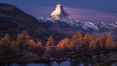 Majestic Snow-Capped Mountain Surrounded by Autumn-Foliaged Forest and Calm Reflections.