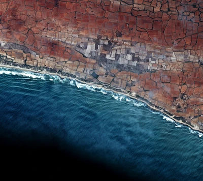 Aerial view of coastal land meeting the ocean, showcasing agricultural patterns and the interplay of terrain and water.