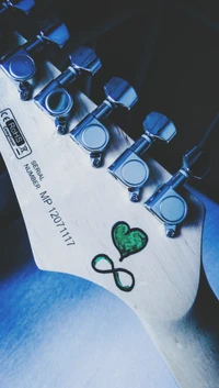 Corazón verde y símbolo de infinito en la cabeza de la guitarra