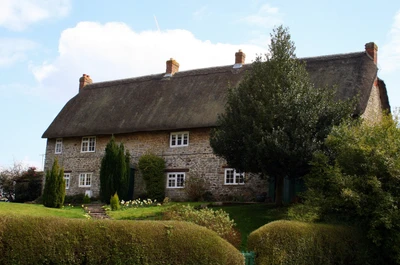 Charmantes Reetdachhaus, umgeben von üppigem Grün und gepflegten Gärten, das die traditionelle englische Landarchitektur zeigt.