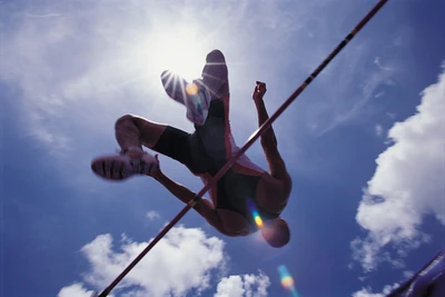 Atleta de salto alto elevándose contra un cielo iluminado por el sol