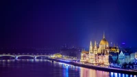 Das ungarische Parlamentsgebäude bei Nacht beleuchtet mit Blick auf die Donau