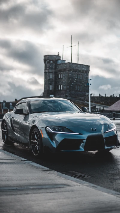 Toyota Supra élégante devant une tour historique sous un ciel dramatique.