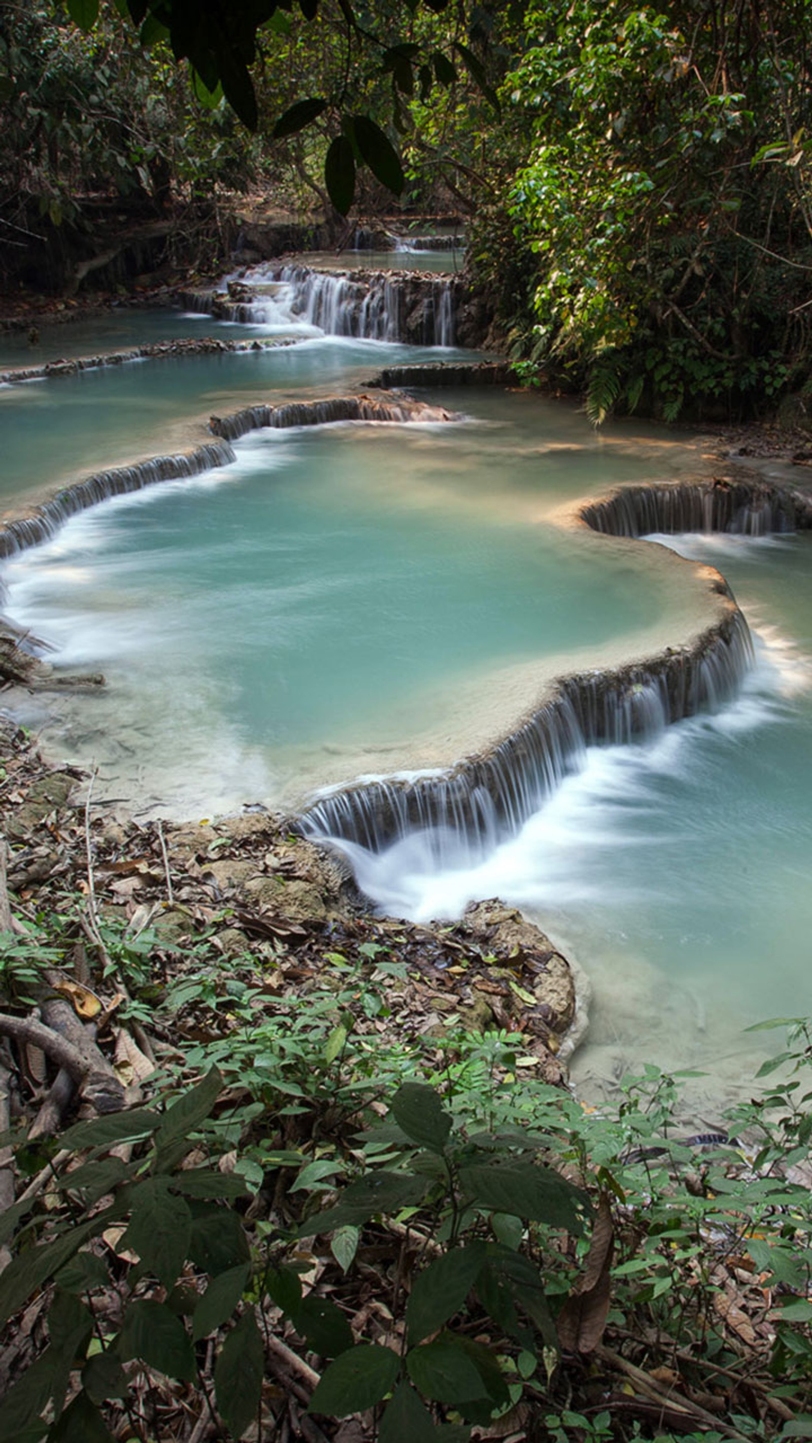 There is a small waterfall that is flowing down the side of a hill (android, drop, falls, iphone, jungle)