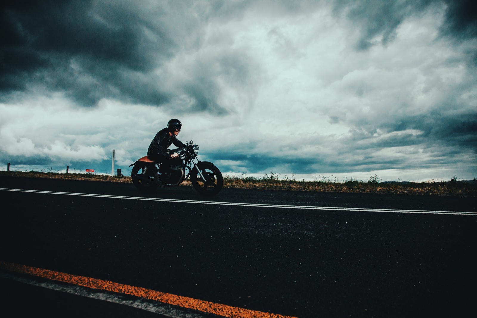 Um homem andando de motocicleta na estrada sob um céu nublado (capacete de motocicleta, motocicleta, nuvem, motociclismo, estrada)