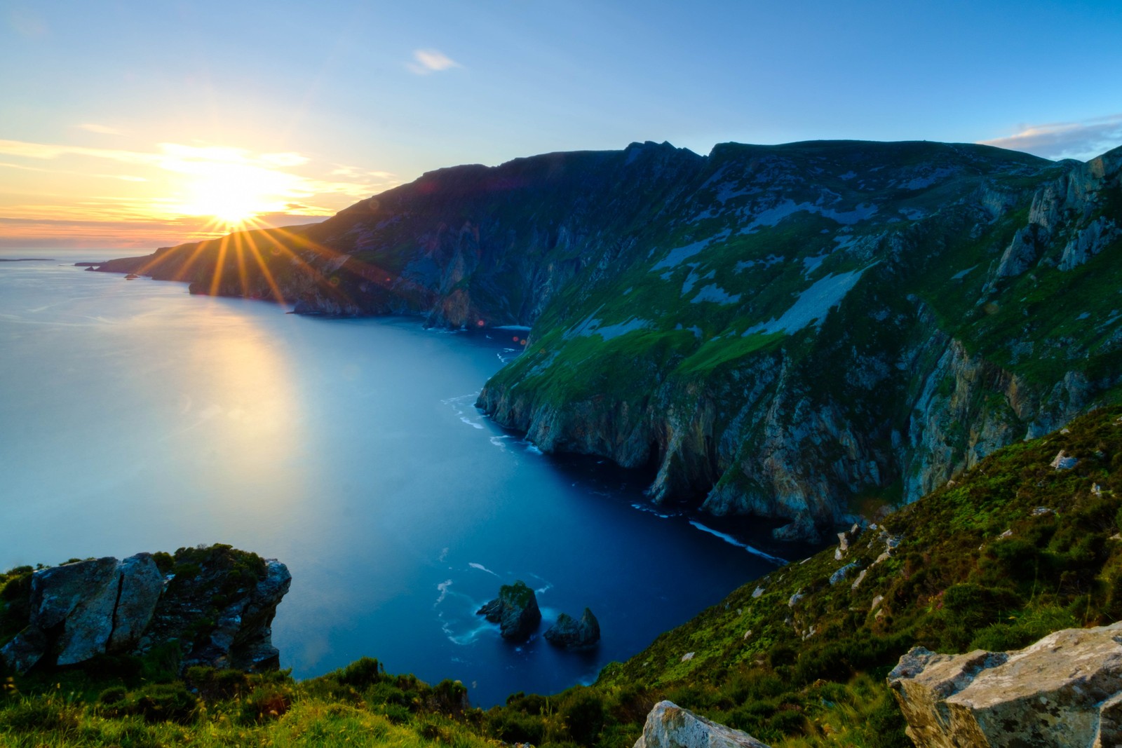 A view of the sun setting over the ocean from a cliff (landscape, coast, sea, headland, cape)