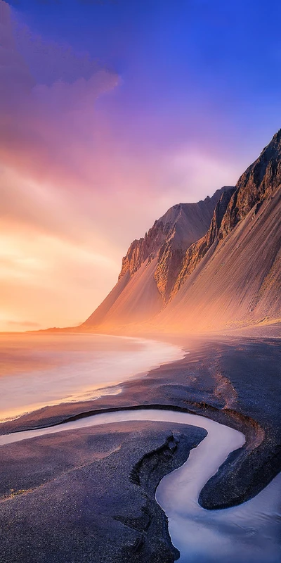 Paysage côtier dramatique au crépuscule avec des formations montagneuses et une rivière sinueuse qui coule vers le rivage.