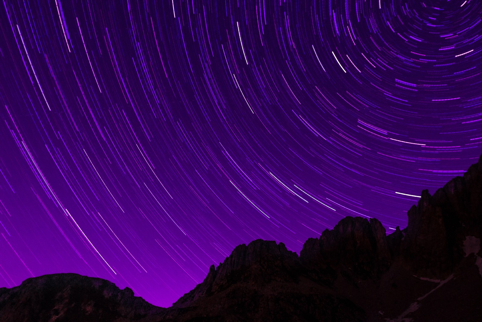 A close up of a mountain with a star trail in the sky (star trails, purple sky, timelapse, night sky, astronomy)