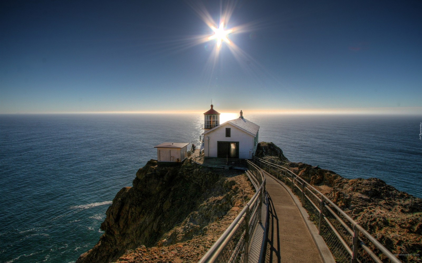 Uma vista de um farol em um penhasco com vista para o oceano (farol, mar, promontório, horizonte, costa)